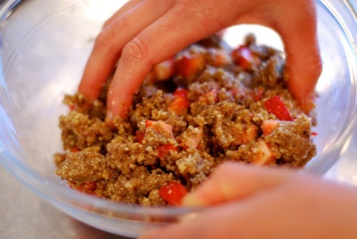 A hand is mixing together the ingredients for strawberry energy bites