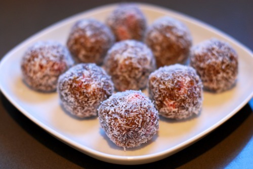 A square white plate with coconut covered strawberry energy bites
