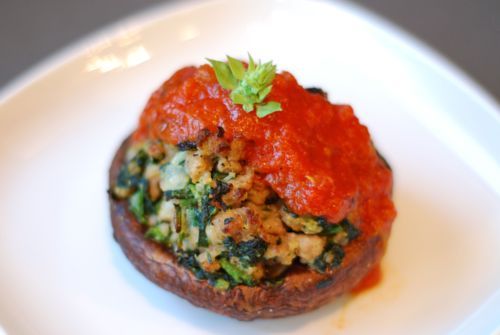 A sausage and spinach stuffed portobello mushroom topped with a dollop of marinara sauce.