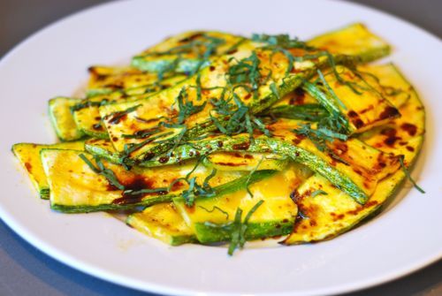 Grilled zucchini on a plate topped with chiffonade pieces of basil.