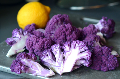 A trimmed purple cauliflower on a cutting board with a lemon.