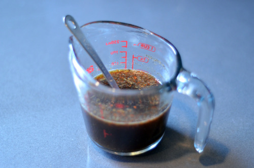 The marinade for the bacon-wrapped tuna in a glass measuring cup with a spoon inside.