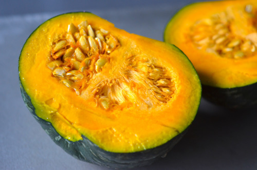 A raw kabocha squash is cut in half, exposing the seeds in the center