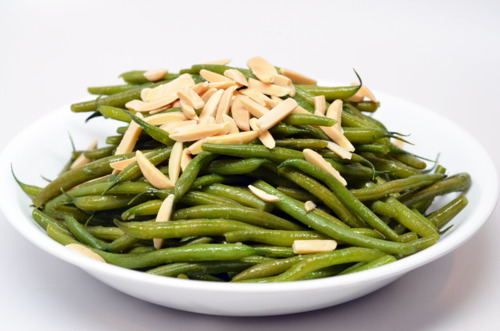 A plate of microwaved green beans in a white bowl topped with slivered almonds.