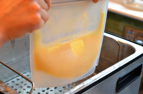 Someone dunking a sous vide bag with scrambled eggs into the sous vide machine to cook.