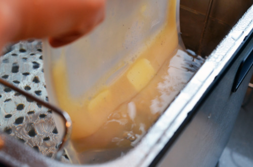 Someone dunking a sous vide bag with scrambled eggs into the sous vide machine to cook.