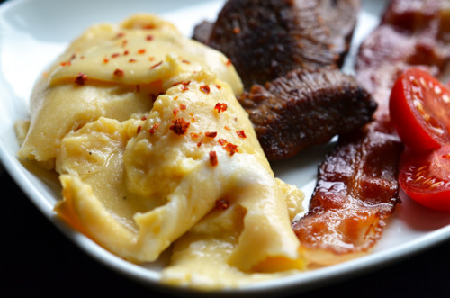 Sous vide scrambled eggs on a plate with breakfast meats and sliced tomatoes.