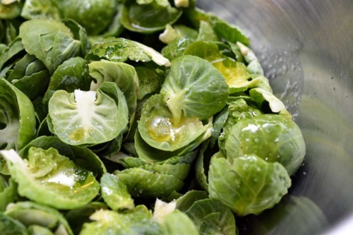 Mixing the Brussels sprouts leaves with oil and salt in a metal bowl.