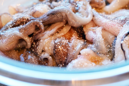 Salt and pepper added to a bowl of raw shrimp for grilled calamari.