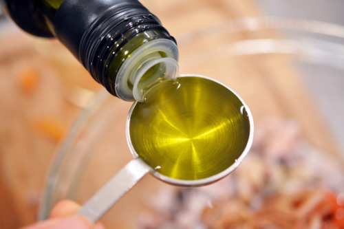 Someone measuring out olive oil that is to be added to the bowl of grilled calamari.