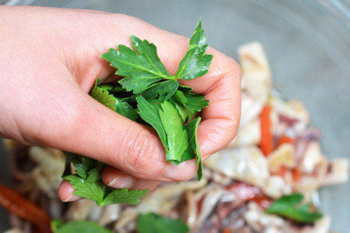 Someone adding parsley to the bowl of grilled calamari with roasted red peppers.