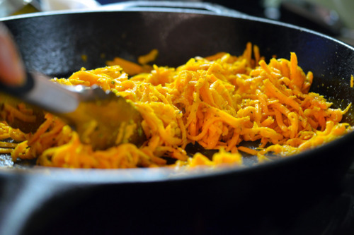 A cast iron skillet with sweet potato hash is almost finished cooking.