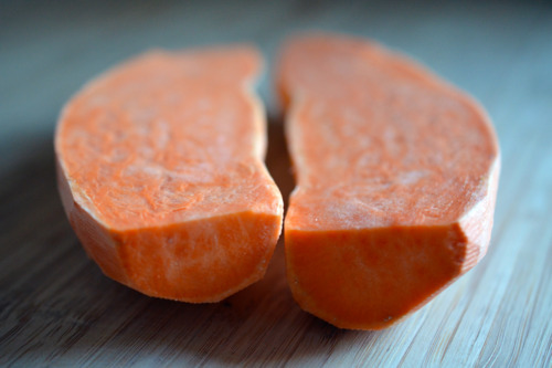 A side shot of a peeled sweet potato cut in half on a wooden cutting board.