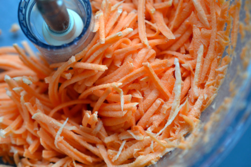 An overhead shot of an open food processor with shredded sweet potatoes inside.