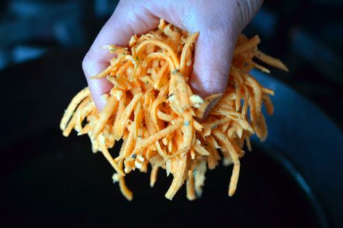 A hand is adding the seasoned sweet potatoes to a cast iron skillet.