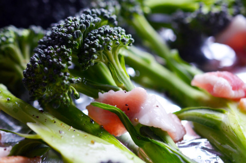 Close up of raw broccoli and bacon bits on a rimmed baking sheet.