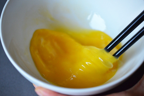 Someone whisking the eggs and fish sauce in a bowl with chopsticks.