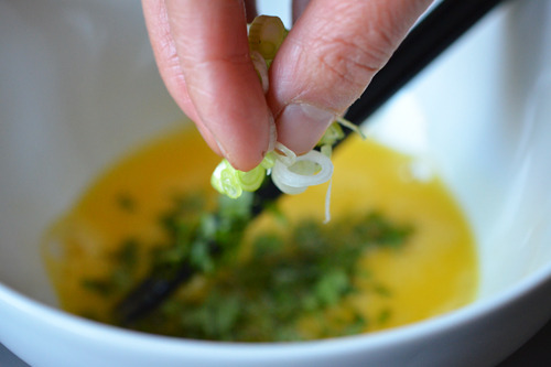 Adding the cilantro and scallions to the bowl of mixed eggs.