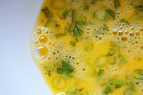 An overhead shot of mixed eggs in a bowl with herbs.