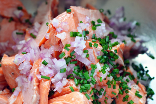 Flaked salmon in a bowl with shallots, chives, and salt and pepper.
