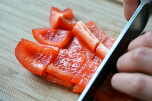 Someone chopping up the red bell pepper pieces into smaller chunks.