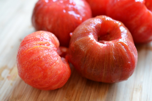 Cored, peeled and boiled tomatoes on a cutting board.