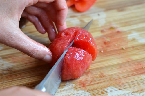 Someone quartering the cooked, cored, and skinned tomatoes.