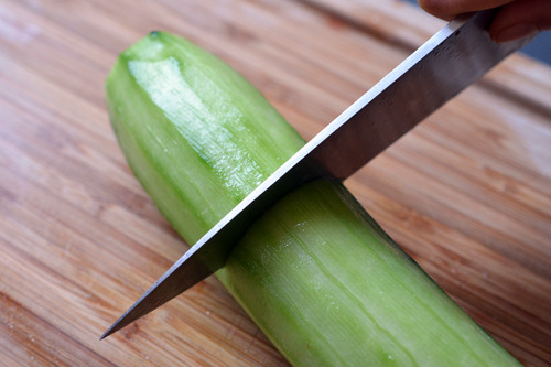 Someone cutting a peeled cucumber on a cutting board.