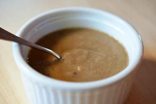 A small white ramekin filled with easy paleo herb gravy with a spoon in the bowl.