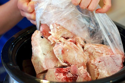 Someone dropping beef bones into a slow cooker for a beef bone broth recipe.