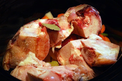 A close up of the beef bones in the slow cooker with bay leaves, salt, and vinegar drizzled over.