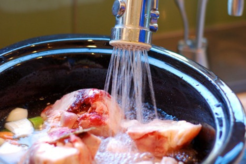 Someone adding water to a slow cooker that is filled with beef bones.