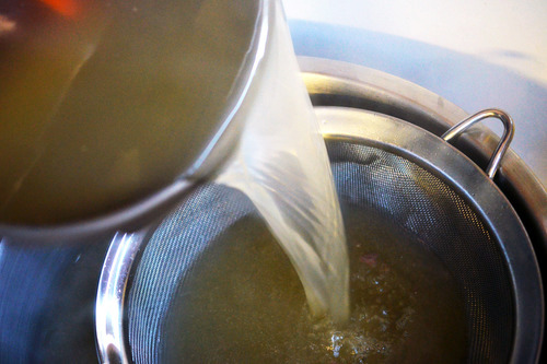 Someone pouring beef bone broth made from the slow cooker through a mesh sieve.