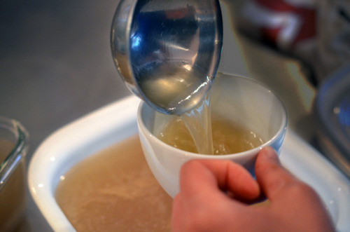 Someone ladling out some beef bone broth into a cup.