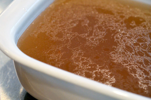 Homemade beef bone broth fills a white tupperware.