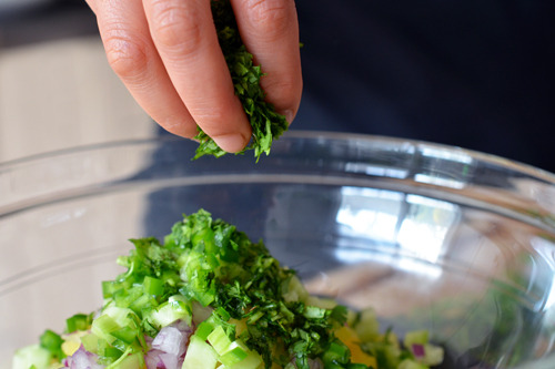 Someone sprinkling on chopped cilantro in a bowl for spicy pineapple salsa.