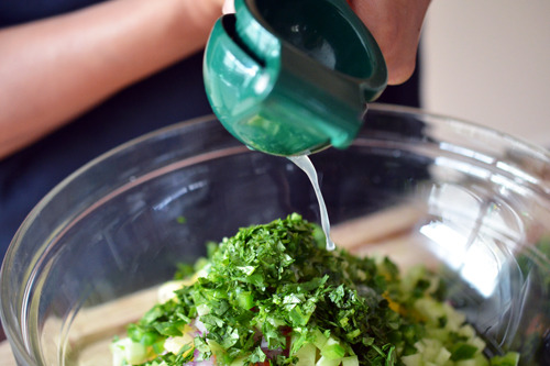 Someone squeezing lime into a bowl with the ingredients for spicy pineapple salsa.
