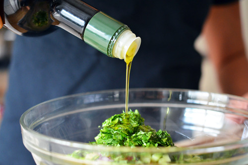 Someone pouring in oil into a bowl with the ingredients for spicy pineapple salsa.