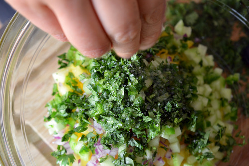 Someone sprinkling salt into a bowl with the ingredients for spicy pineapple salsa.