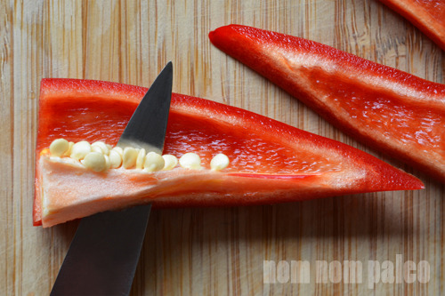 Using a paring knife to remove the seeds and veins from a red jalapeño pepper.