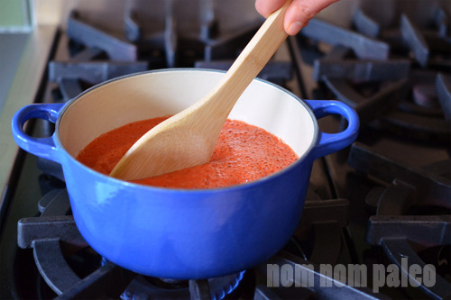 Homemade Paleo Sriracha simmering and being stirred in a saucepan.